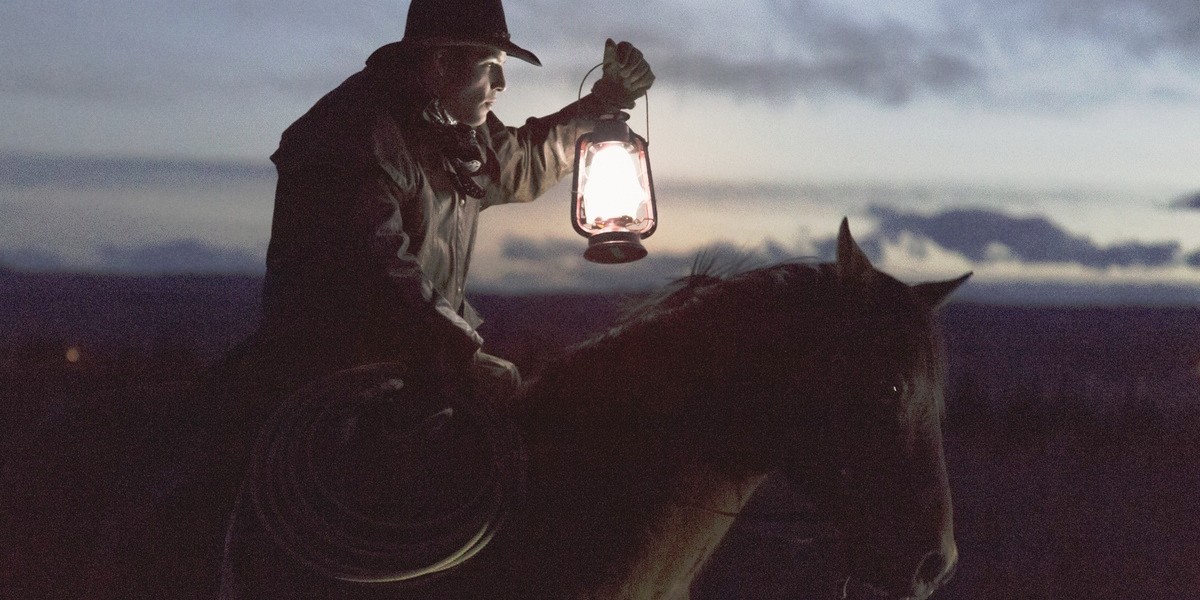 Cowboy riding horse at night carrying lantern